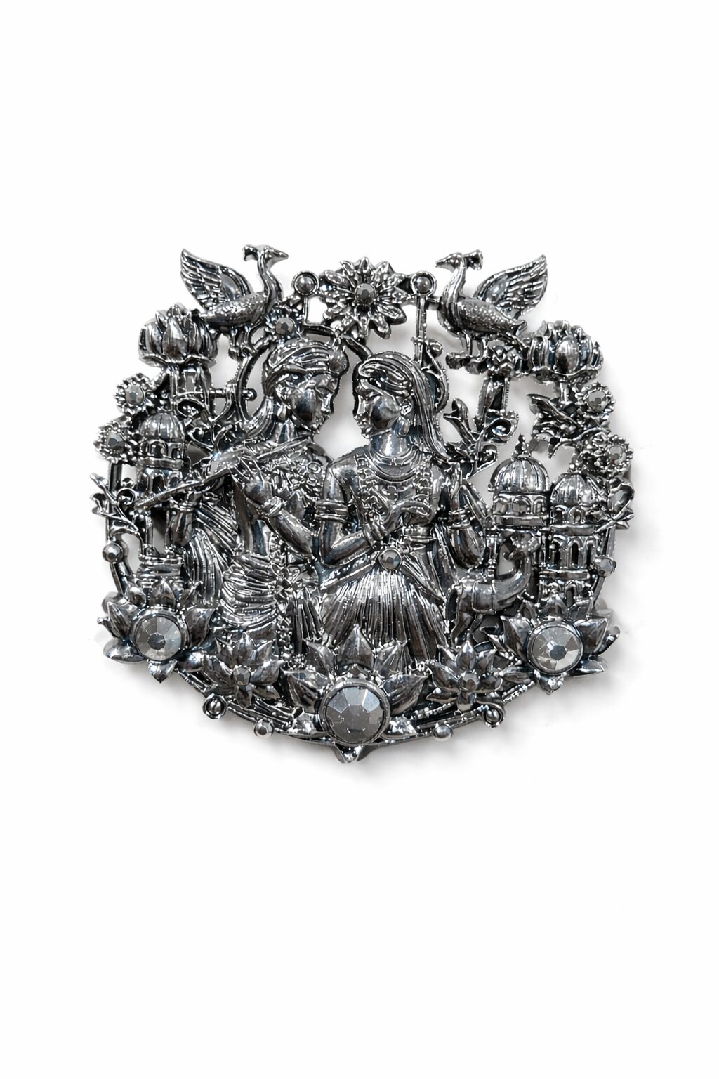 Silver-tone Radha Krishna brooch featuring intricate floral motifs, peacocks, lotus flowers, and crystal embellishments, ideal for weddings and festive occasions.