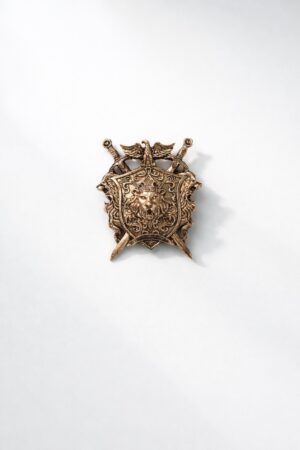 Antique gold lion crest shield brooch featuring a crowned lion emblem, crossed swords, and intricate royal detailing, ideal for wedding and ceremonial wear.