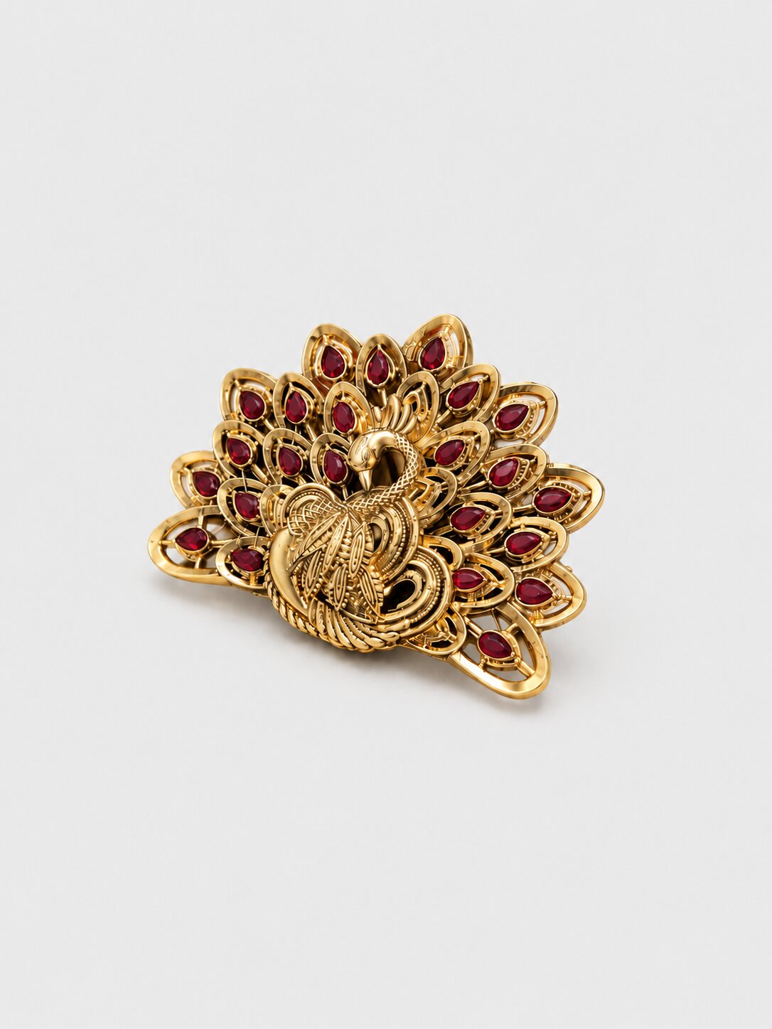 Gold-tone peacock-shaped brooch featuring intricate filigree detailing and red teardrop gemstones arranged in a fan-shaped feather design, displayed on a light gray background.