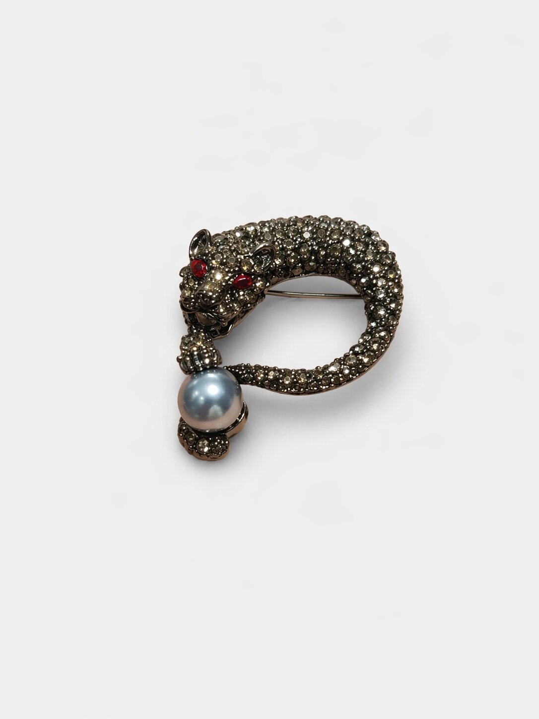 Luxury panther brooch with crystal-studded body, red gemstone eyes, and a pearl accent in a dark antique metal finish.