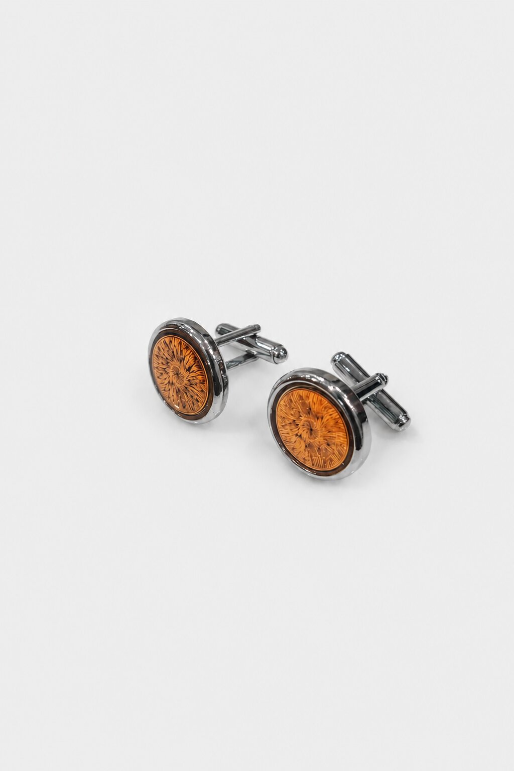 Round silver-tone cufflinks with amber floral pattern center and polished metal finish.
