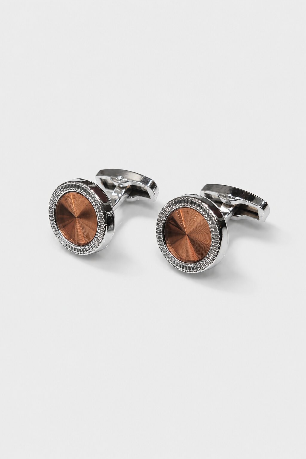 Round silver-tone cufflink with brushed copper center accent in a luxury formal setting.