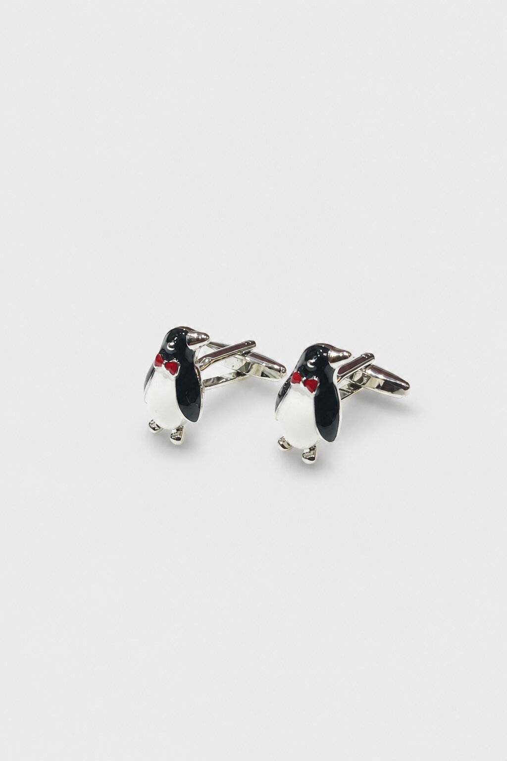 Penguin-shaped cufflinks with black and white enamel detailing and red accent bow tie design.