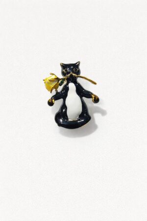 Black and white enamel cat brooch holding a yellow rose with gold-tone details.
