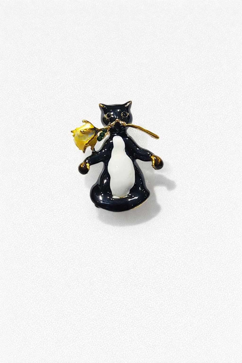 Black and white enamel cat brooch holding a yellow rose with gold-tone details.