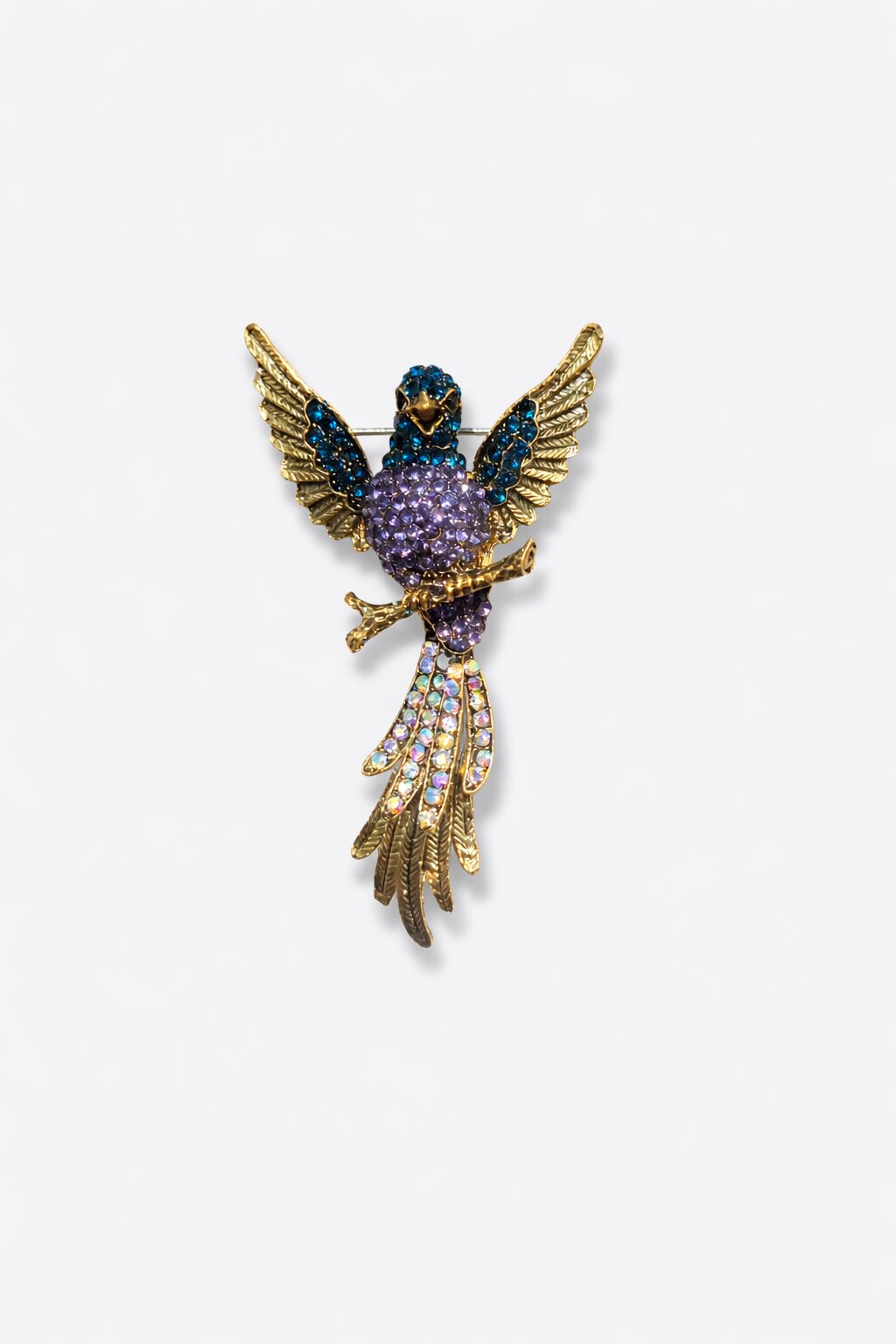 Gold-tone bird brooch adorned with blue and lavender crystals, featuring detailed wings and a sparkling crystal tail.